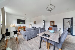Una sala de estar moderna con un sofá gris, una mesa de comedor de madera y un televisor montado en la pared.