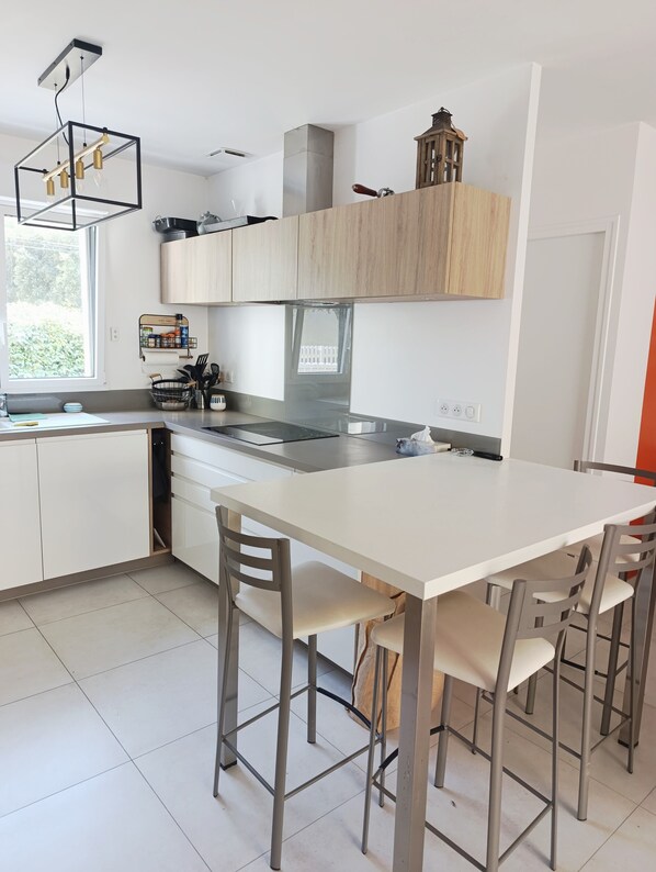 A modern kitchen with white cabinets, a central island, and a dining area with chairs.