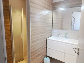 Une salle de bain moderne avec un mur en bois, un lavabo blanc, un miroir et une poubelle.