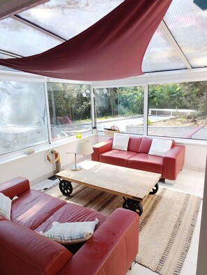 A modern living room with a red sofa, a wooden coffee table, and a large window overlooking a garden.