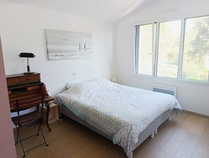 Un dormitorio con cama, escritorio con lámpara, un cuadro y una ventana.