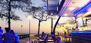 Uma área de refeições ao ar livre com mesas e cadeiras, um bar com balcão e vista para a praia.