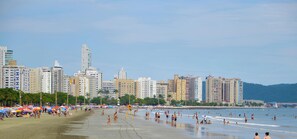 Uma praia com pessoas, guarda-sóis e edifícios altos ao fundo.