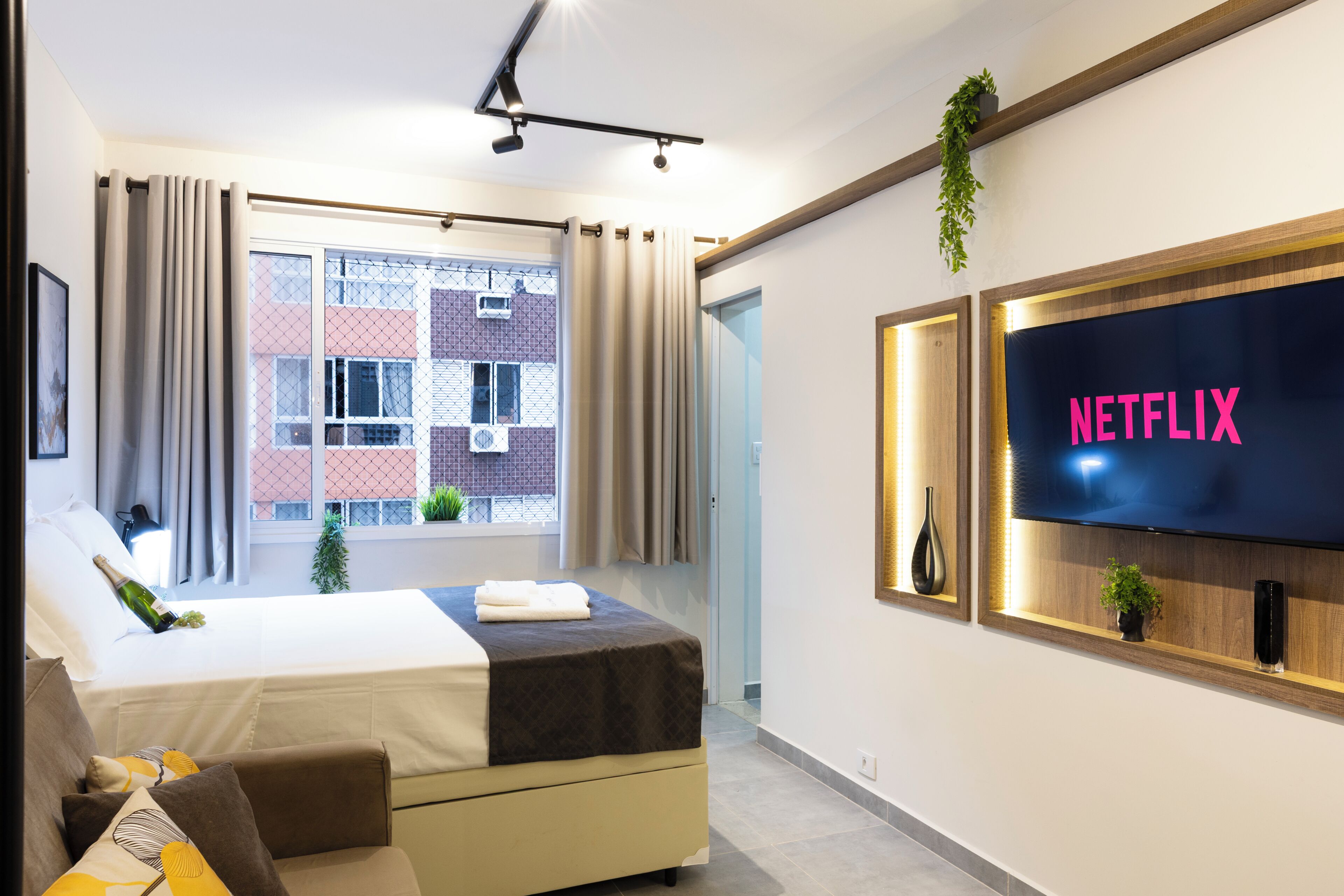 Een hotelkamer met een bed, een televisie, een raam met gordijnen en uitzicht op gebouwen.