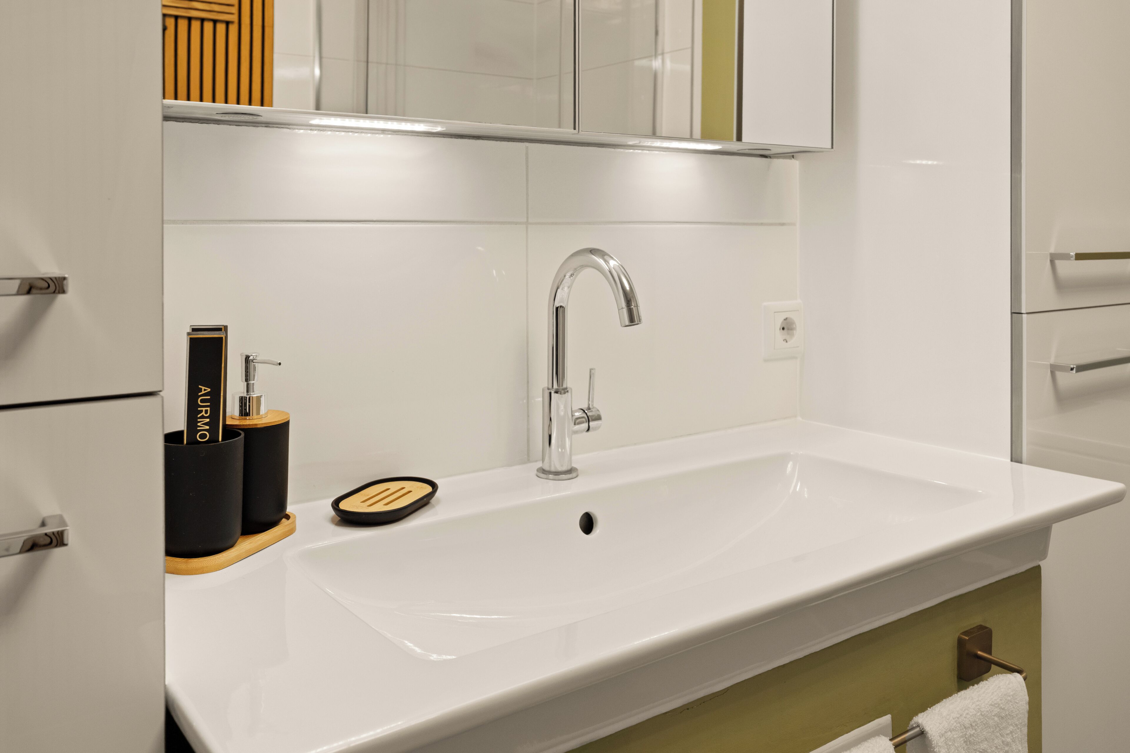 Une salle de bain moderne avec un lavabo blanc, un robinet chromé et un porte-savon en bois.