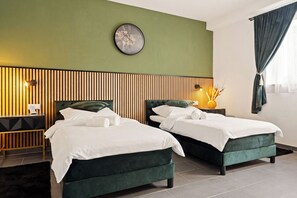 Une chambre d’hôtel avec deux lits, une horloge murale, une tête de lit en lattes de bois, une table de chevet avec une lampe et une fenêtre avec des rideaux.