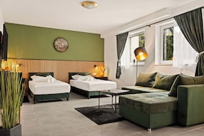A modern hotel room with two beds, a green sofa, a small table, a lamp, and a large window with curtains. - Modo Apartments Erkelenz | Pool and sauna (Erkelenz)