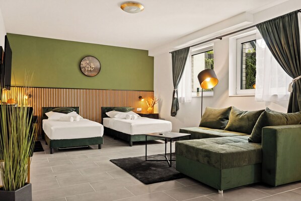 Une chambre d’hôtel moderne avec deux lits, un canapé vert, une petite table, une lampe et une grande fenêtre avec des rideaux.