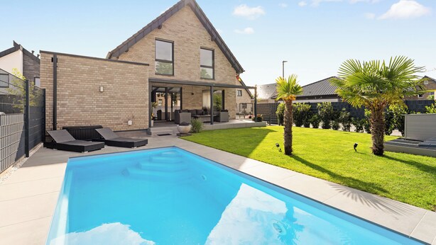 Ein modernes Haus mit Swimmingpool, gepflegtem Rasen und einer Ziegel-Fassade.