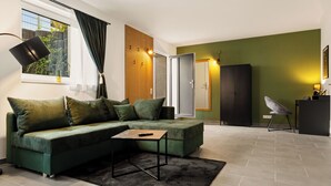 Ein modernes Wohnzimmer mit einem Ecksofa, einem kleinen Tisch und Blick ins Freie durch ein Fenster.