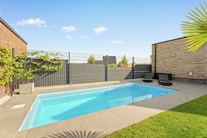 A rectangular swimming pool with a tiled deck, surrounded by a brick wall and a metal fence. - Modo Apartments Erkelenz | Pool and sauna (Erkelenz)