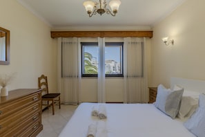 Ein Hotelzimmer mit einem großen Bett, einem Holzschrank, einem Sessel, einem Nachttisch, einer Wandlampe und einem Fenster mit Vorhängen.