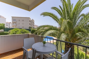 Ein Balkon mit Tisch und Stühlen, einer kleinen Pflanze und Blick auf ein Gebäude und Palmen.