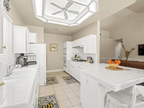 A modern kitchen with white cabinetry, a coffee maker, and a dining area with a table and chairs. - 6BR Home | Sleeps 11 | Fireplace +Private Backyard (Fresno)