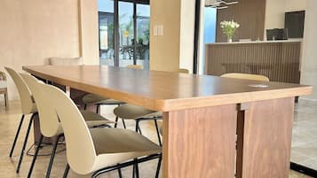 Uma sala de conferências moderna com uma mesa de madeira, cadeiras bege e uma mesa de recepção com uma planta.