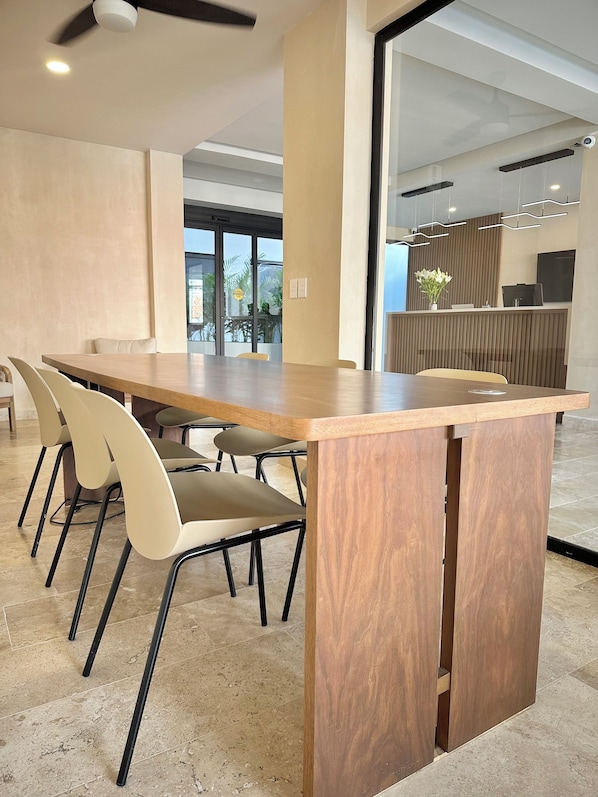 Una sala de conferencias moderna con una mesa de madera, sillas color beige y un mostrador de recepción con una planta.