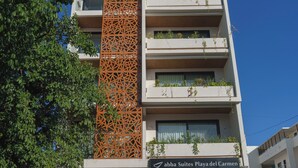 Un hotel de varios pisos con balcones, un panel decorativo vertical naranja y un letrero que dice 'abba Suites Playa del Carmen'.