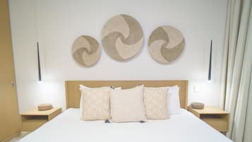 Cama bem arrumada com almofadas estampadas, cabeceira de madeira e três peças de arte tecida na parede.