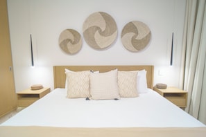 Una cama bien hecha con almohadones estampados, un cabecero de madera y tres piezas de arte tejidas colgadas en la pared.
