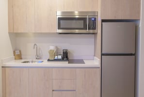 Una cocina con microondas de acero inoxidable, refrigerador, pileta y alacenas de madera.