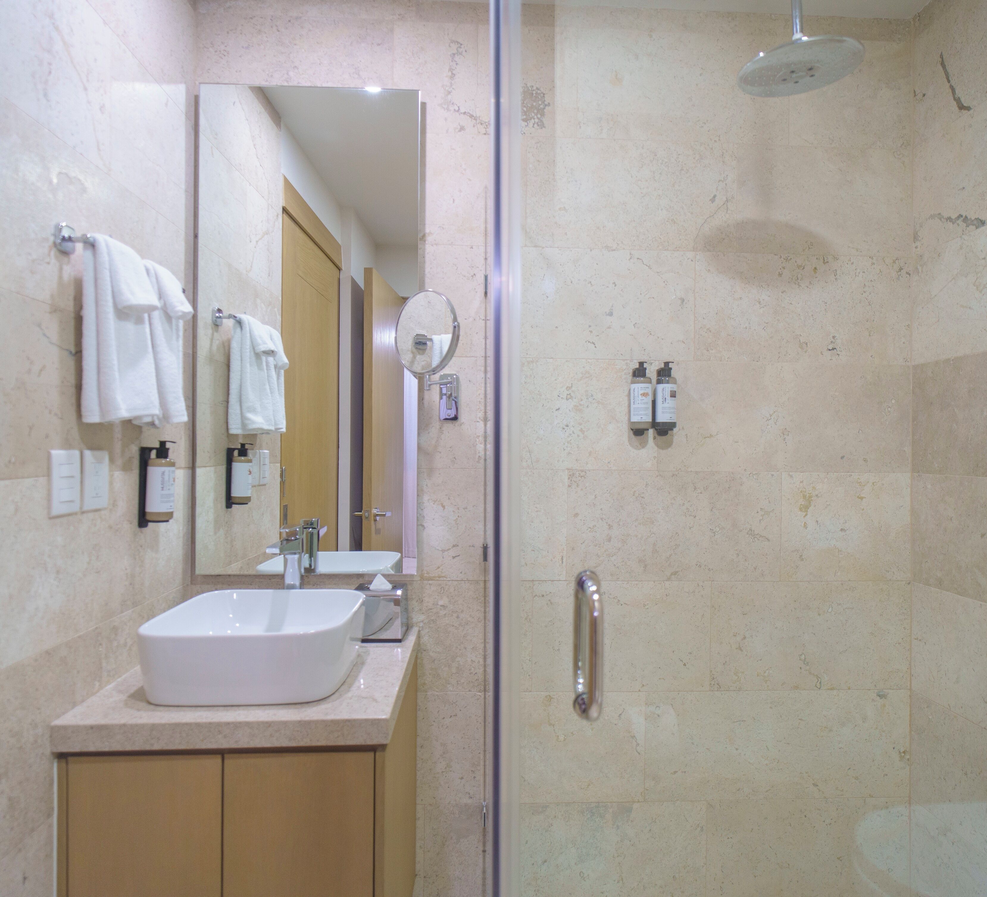 A bathroom with a sink, mirror, towel rack, shower, and toiletries.