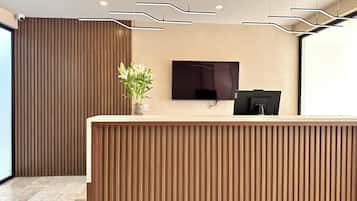 A reception desk with a flat-screen TV, a vase with flowers, and a modern ceiling design.