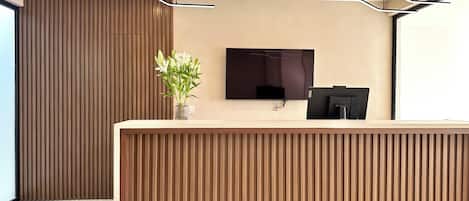 A reception desk with a flat-screen TV, a vase with flowers, and a modern ceiling design.