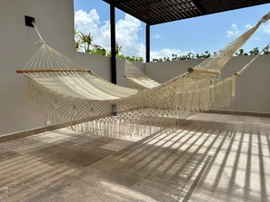 A hammock setup in a covered outdoor area with a tiled floor and a view of the sky.