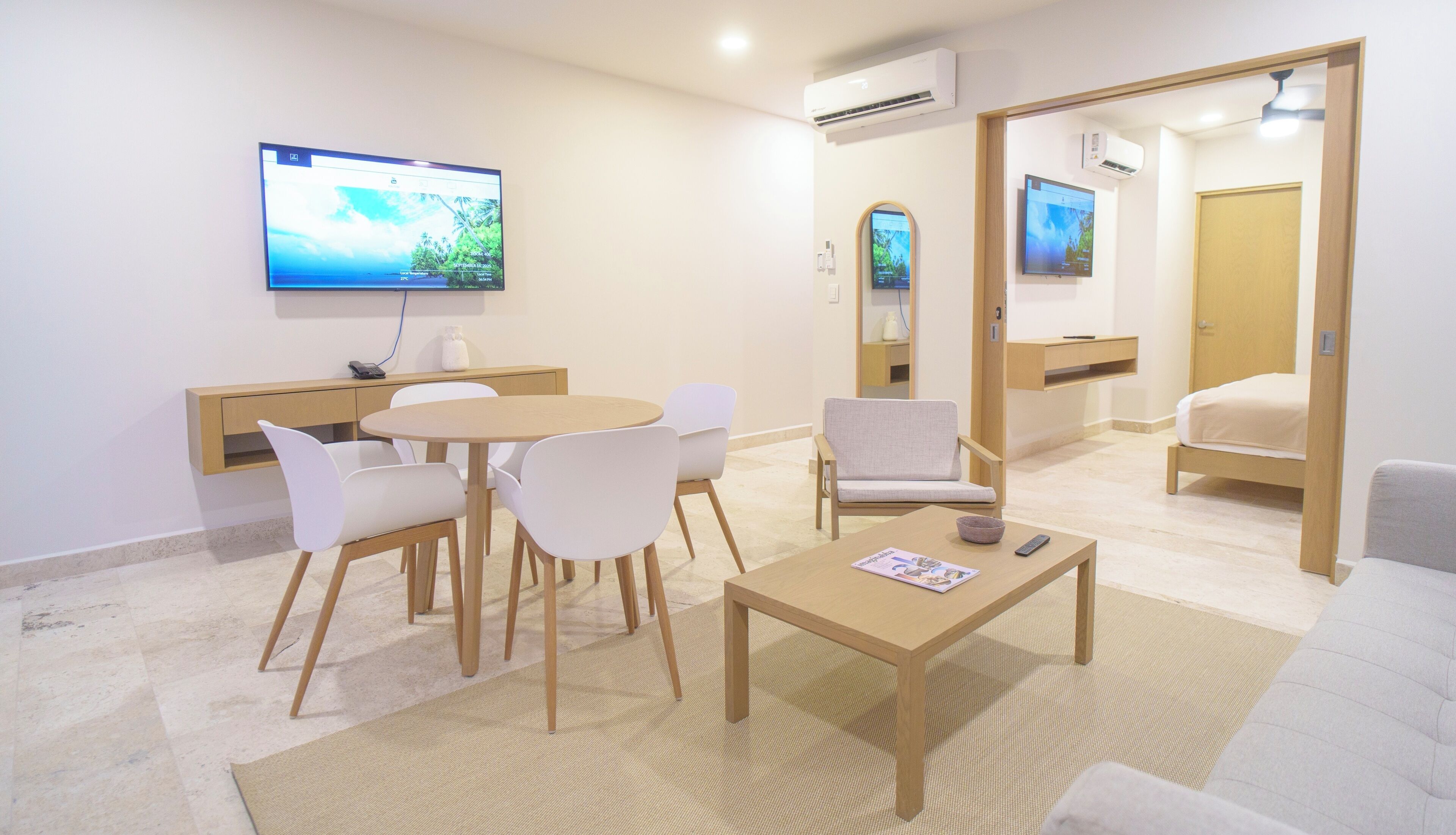 Una habitación de hotel moderna con zona de comedor, sofá, televisión y un mueble de madera.