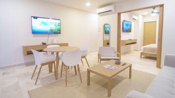 Una habitación de hotel moderna con zona de comedor, sofá, televisión y un mueble de madera.
