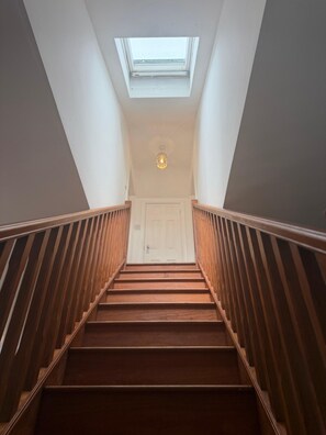 A staircase with wooden railings leading to a landing with a skylight and a door. - Holiday Home Sleeps 8 With Garden (Warwick)