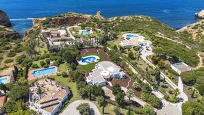 Vista aerea di un resort costiero con diverse piscine, un edificio centrale imponente e vegetazione circostante.