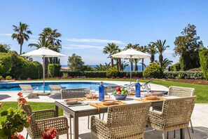 A poolside dining area with wicker chairs, a table set for a meal, and umbrellas providing shade. - Casa Seteais (Carvoeiro)