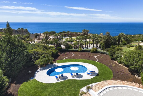 A landscaped pool area with a view of the ocean. - Casa Seteais (Carvoeiro)