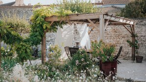 A garden with a pergola, stone wall, and a table with chairs.