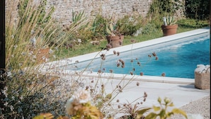 A pool area with a stone wall, potted plants, and a pergola with greenery. - Maison Tassigny (Meursault)