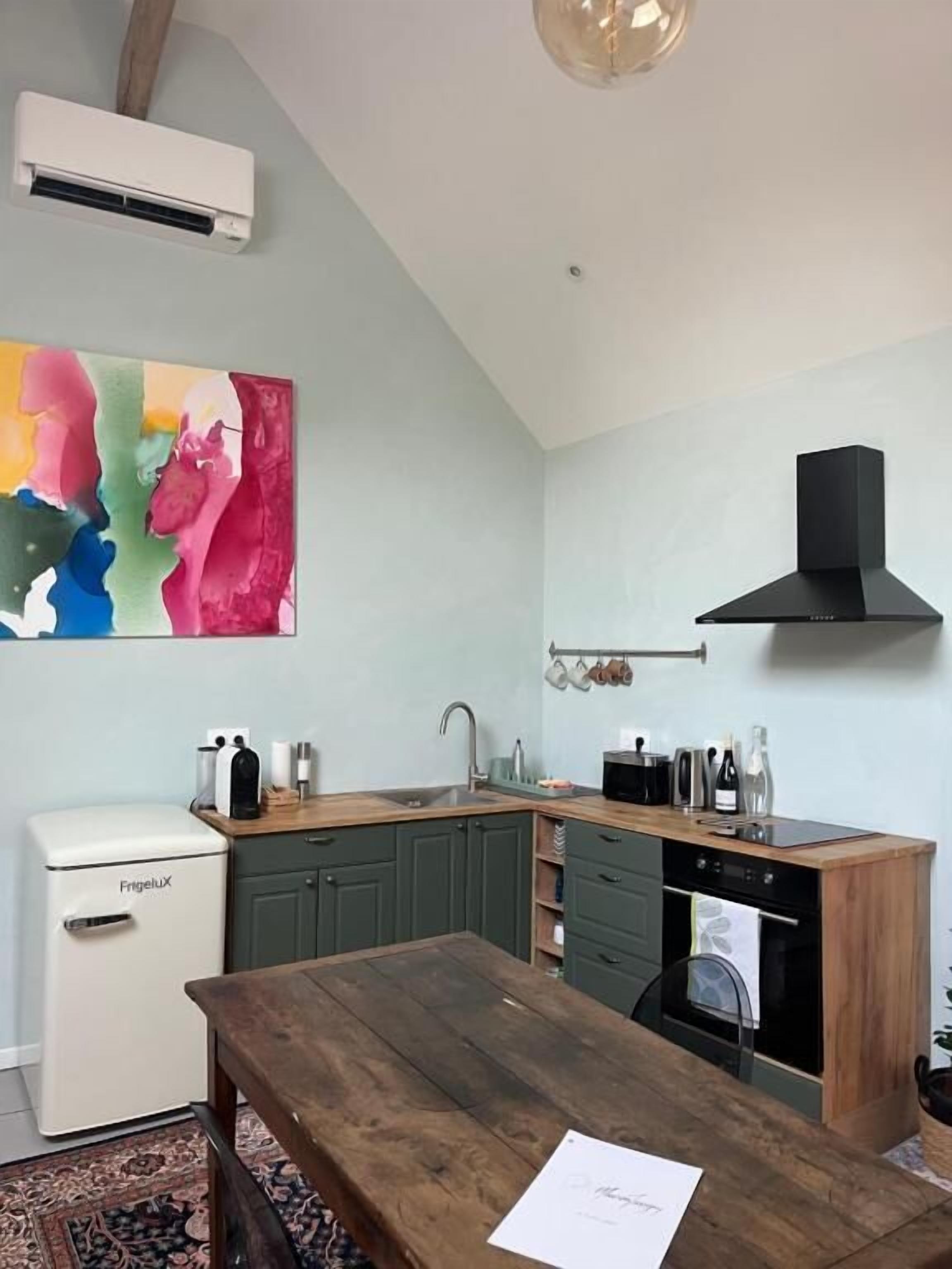 A compact kitchen with a wooden table, a white appliance, and a colorful abstract painting.