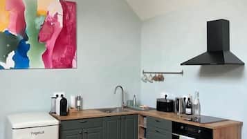 A compact kitchen with a wooden table, a white appliance, and a colorful abstract painting.