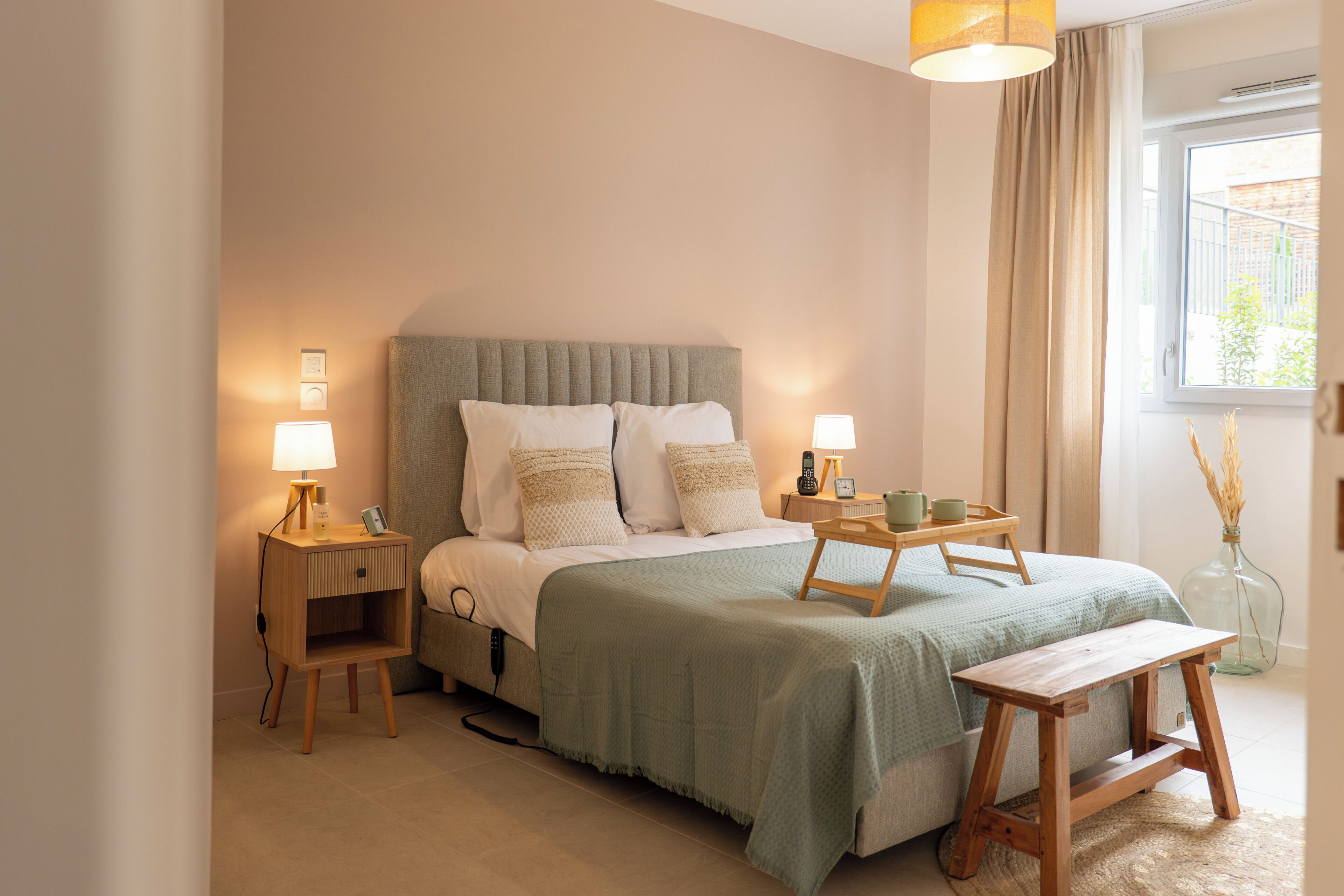 A bedroom with a bed, bedside tables, lamps, a bedside plant, and a window with curtains.