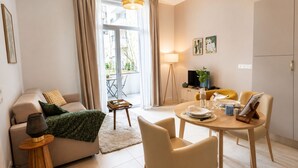 Una sala de estar moderna con un sofá, una mesa de comedor y sillas, una mesita auxiliar y vistas a un área exterior a través de un ventanal.