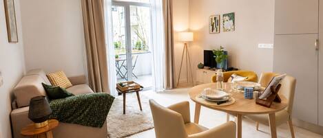 Una sala de estar moderna con un sofá, una mesa de comedor y sillas, una mesita auxiliar y vistas a un área exterior a través de un ventanal.