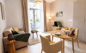 A modern living room with a sofa, dining table, and chairs, a small side table, and a view through a glass door to an outdoor area. - Zenao Appart'hôtels Vichy (Vichy)