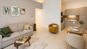 Una sala de estar moderna con un sofá, un sillón, una mesa de centro y un comedor con una mesa preparada para dos.