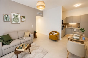A modern living room with a sofa, armchair, coffee table, and dining area with a table set for two. - Zenao Appart'hôtels Vichy (Vichy)