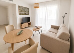 A modern living room with a sofa, a TV, a dining table, and a small coffee table.