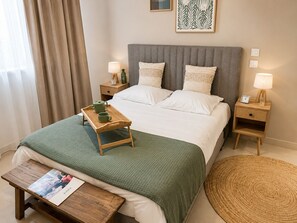 A neatly arranged hotel room with a bed, bedside tables, a tray with tea cups, and a magazine on a side table.