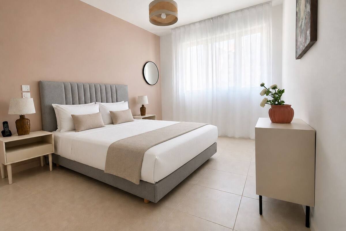 A modern bedroom with a bed, bedside tables, a nightstand, a lamp, a mirror, a potted plant, and a painting on the wall.
