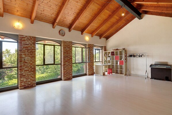 A spacious room with large windows, exposed wooden beams, and a brick wall. - Casa 'Centomila Volte Benvenuti' (Tigliole)