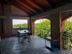 A covered patio with a table and chairs, brick walls, and a view of greenery. - Holiday Home 'Casa Centomila Volte Benvenuti' with Private Terrace (Tigliole)