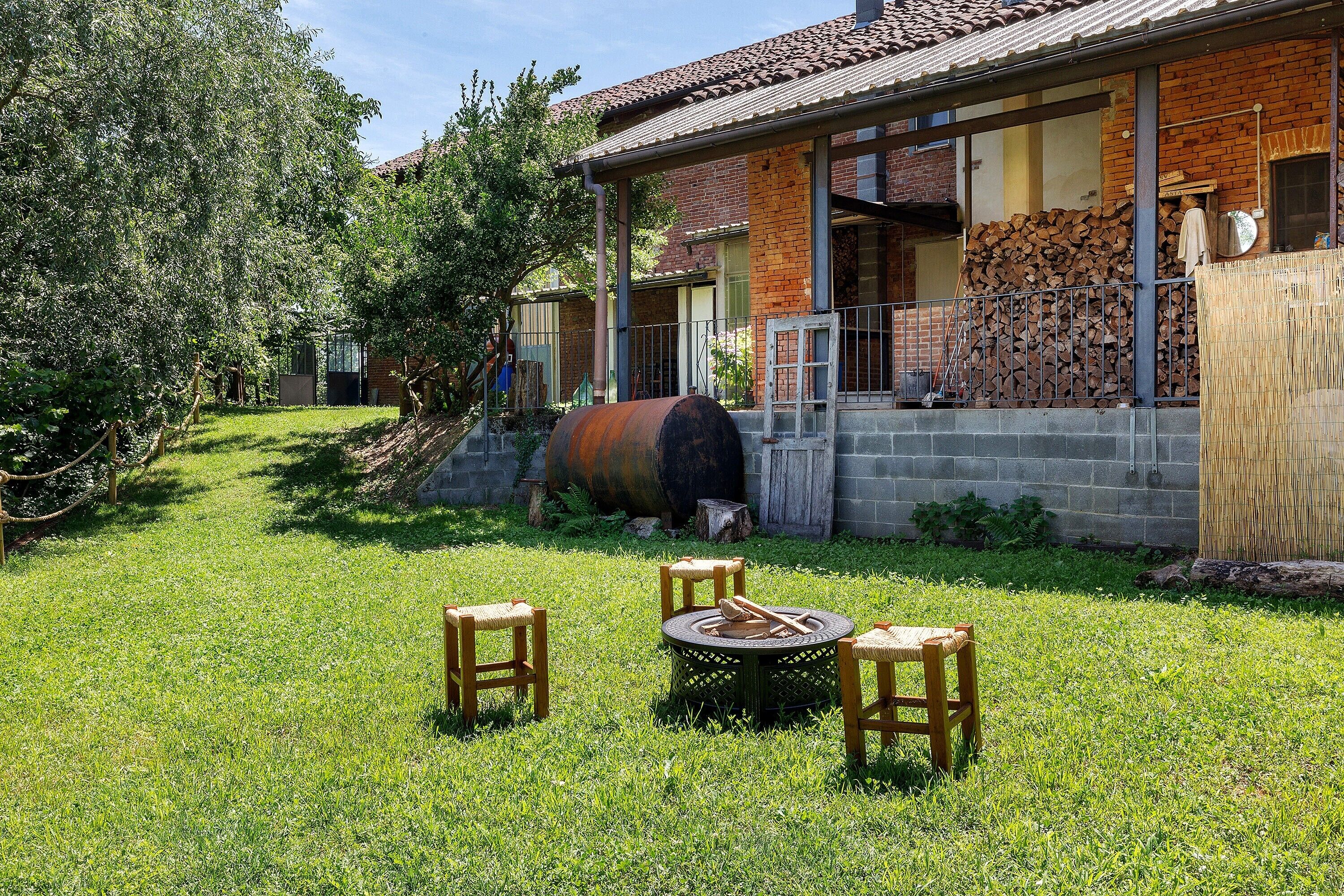 Ein Garten mit Feuerstelle, Sitzgelegenheiten und einem Haus mit Backsteinfassade und großen Fenstern.